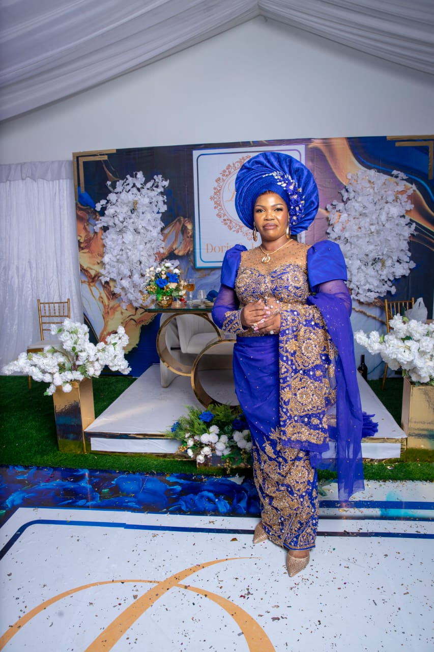 Bride in royal blue and gold beaded gown with matching gele on wedding stage