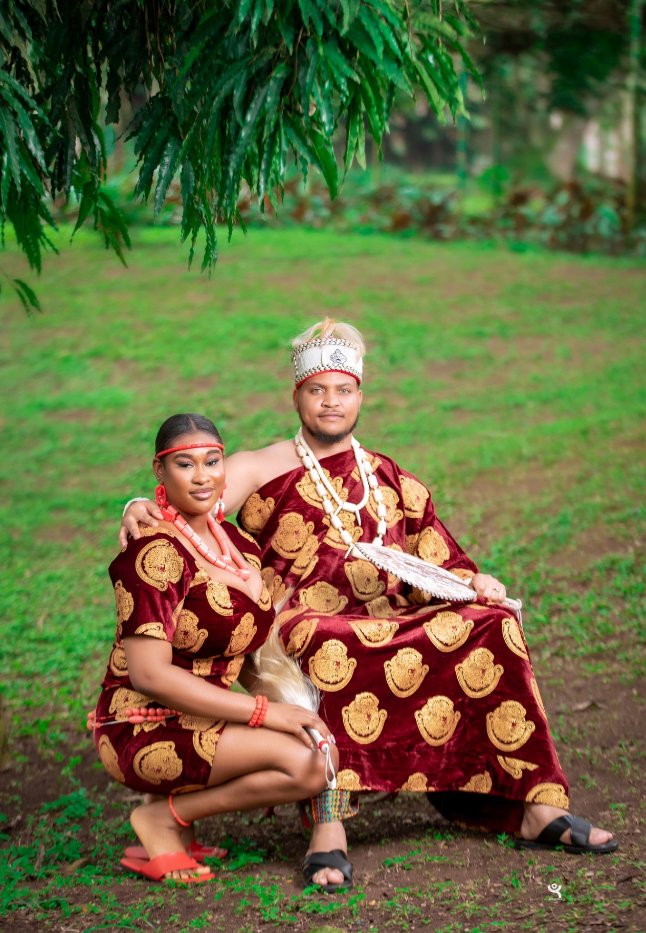 Couple in burgundy traditional attire seated outdoors for engagement portrait
